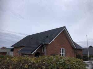 Rødt murstenshus med sort tegltag og buske