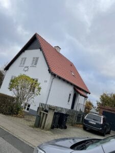 Hvidt hus med rødt tag og bil.