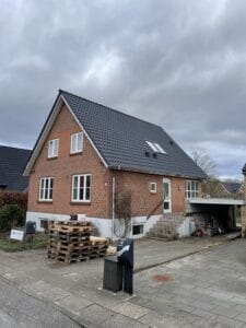 Rødt murstenshus med gråtag og indkørsel i Danmark.